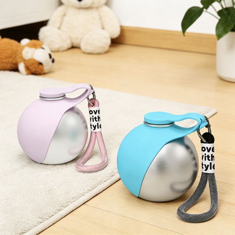 The spherical stainless steel dog water bottle in pink and cyan, both with wrist straps, standing on a wooden floor